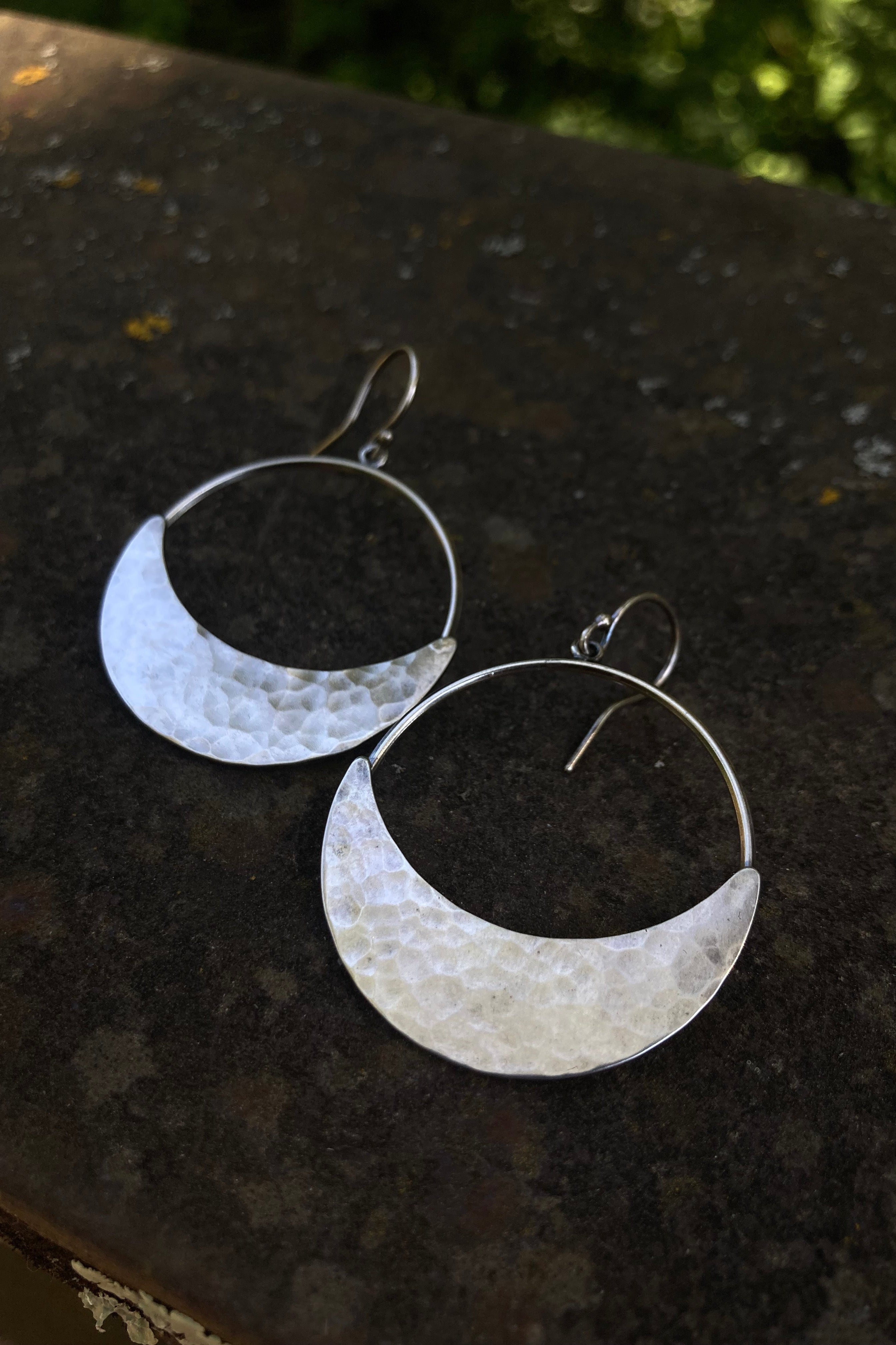 Silver hoop earrings with a hammered finish on a dark surface.