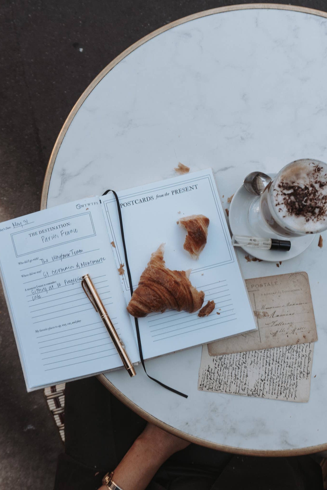 Open notebook with a croissant and coffee on a marble table