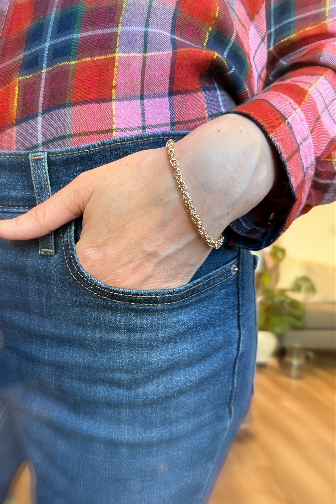 Person wearing blue jeans and a red plaid shirt with a gold bracelet.