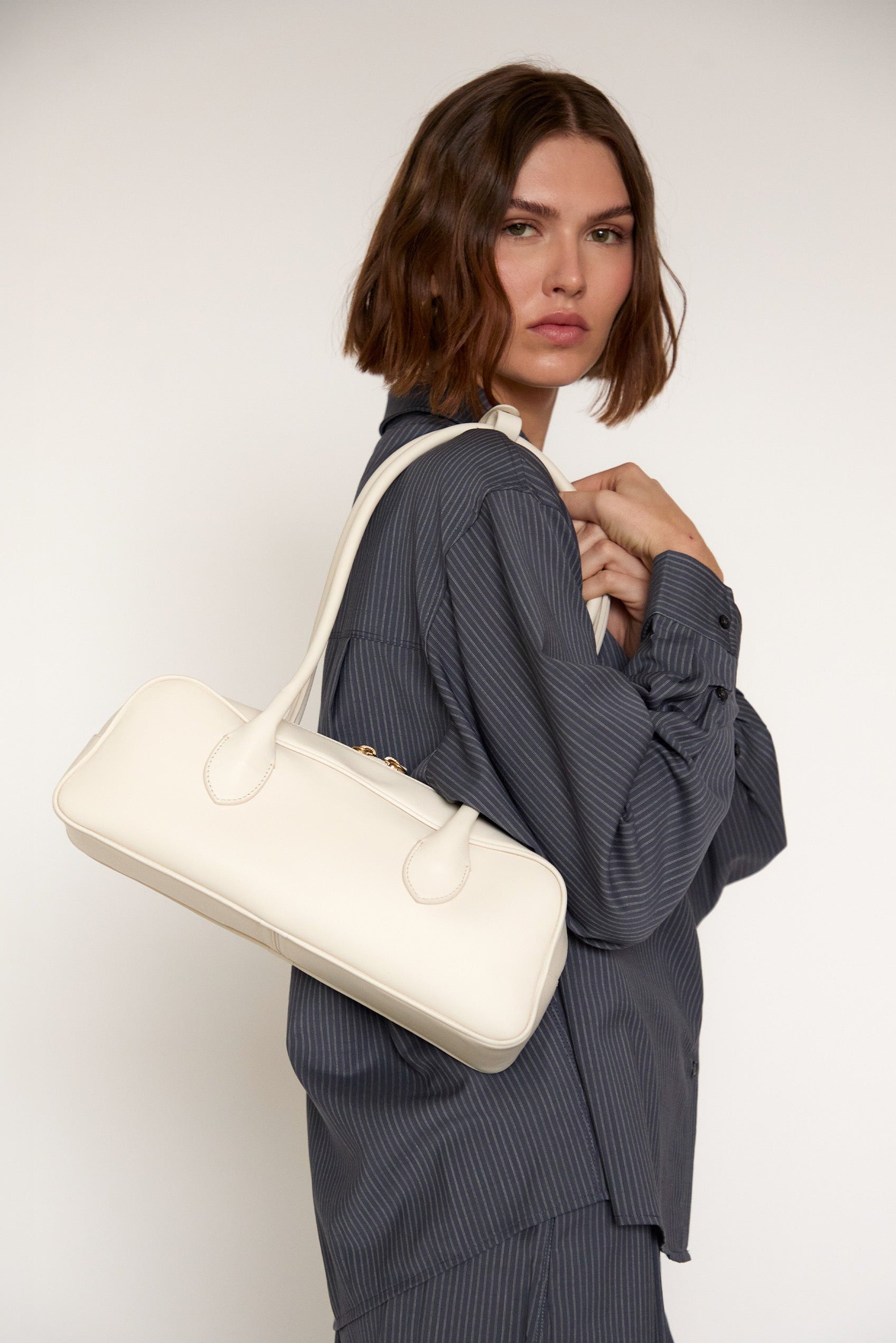 Woman holding a white handbag against a plain background