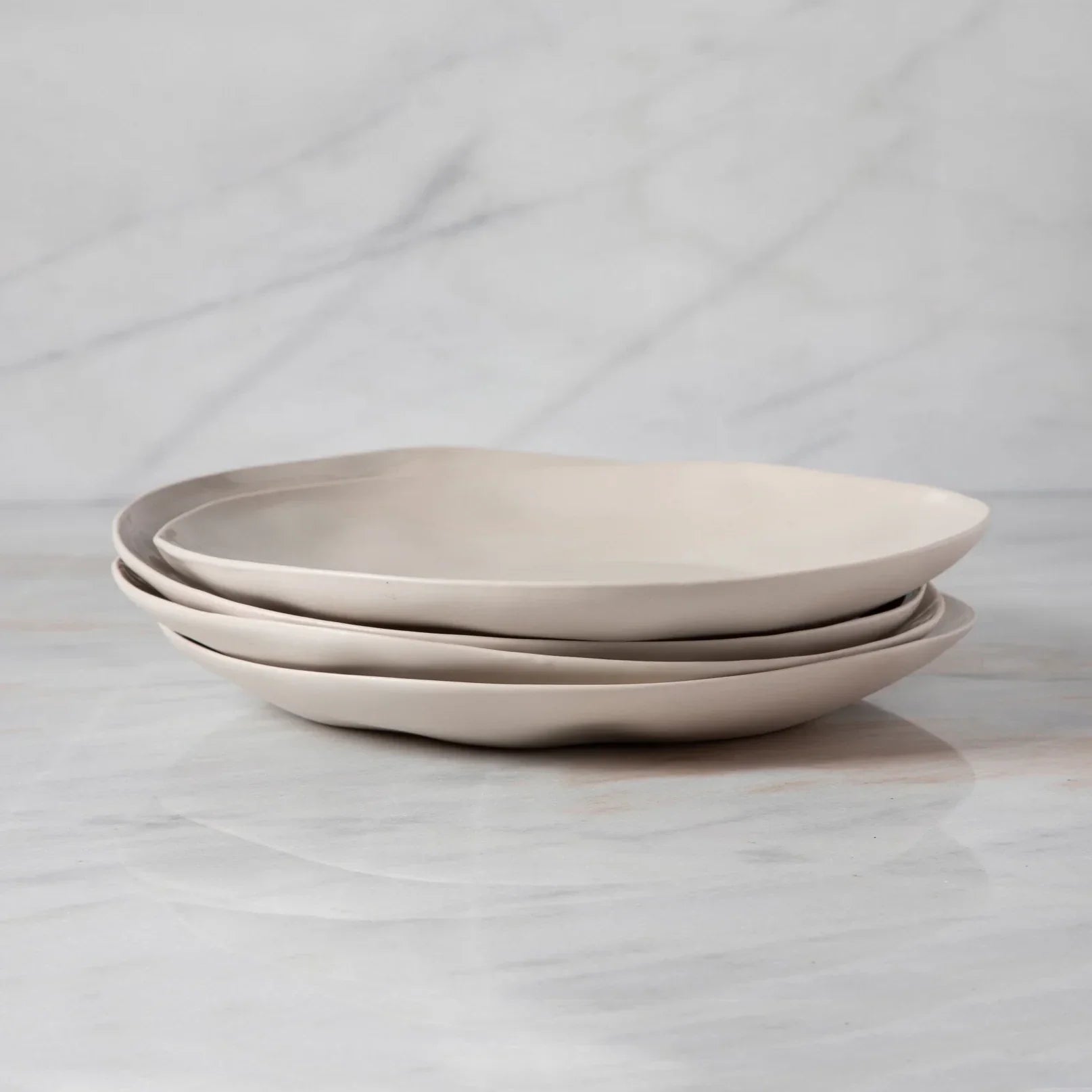 Set of three beige ceramic plates stacked on a light gray surface with a light gray background