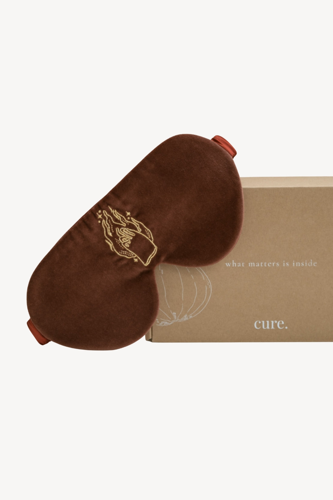 A crimson velvet sleep mask with gold embroidered details, shown next to its kraft paper packaging box on a light gray background.