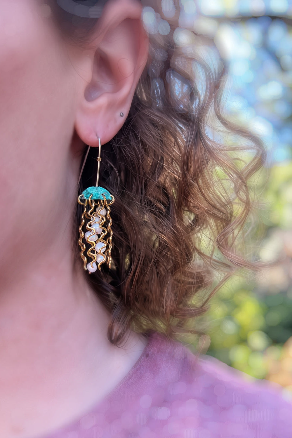 Close-up of a person wearing a gold earring with a turquoise stone outdoors.