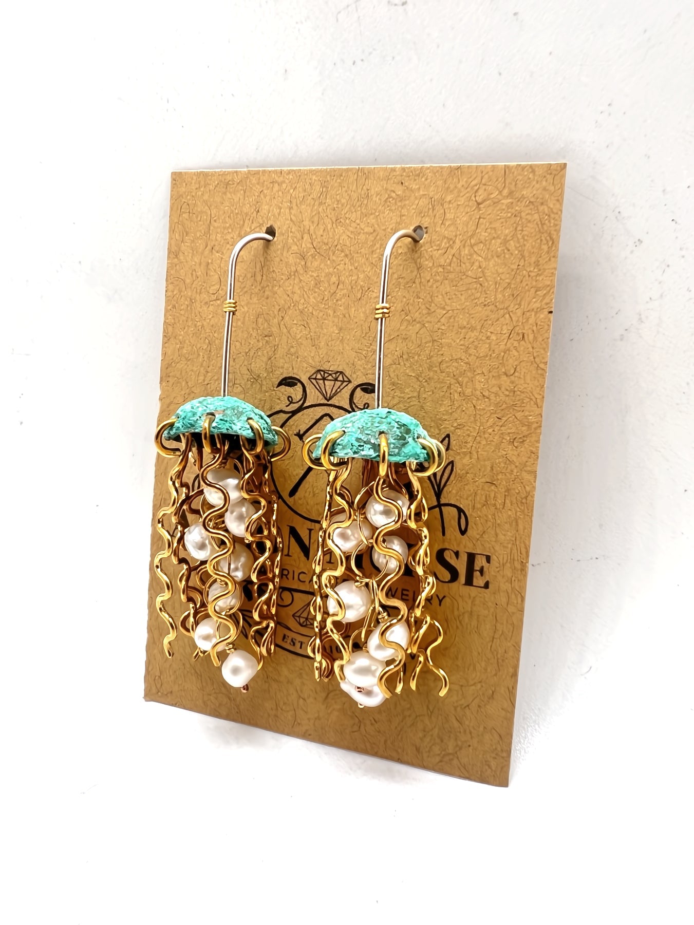 Gold and turquoise earrings on a brown card with visible brand name.