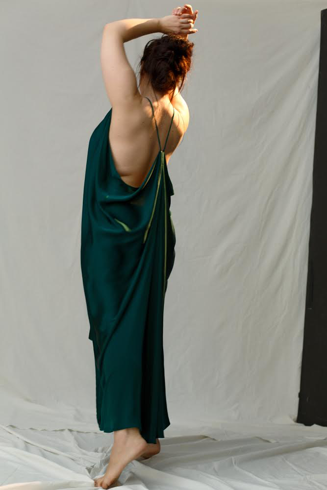 Person wearing a green silk dress with thin straps, standing against a plain background