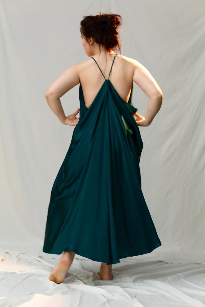 Woman wearing a silk green dress with thin straps on a plain background