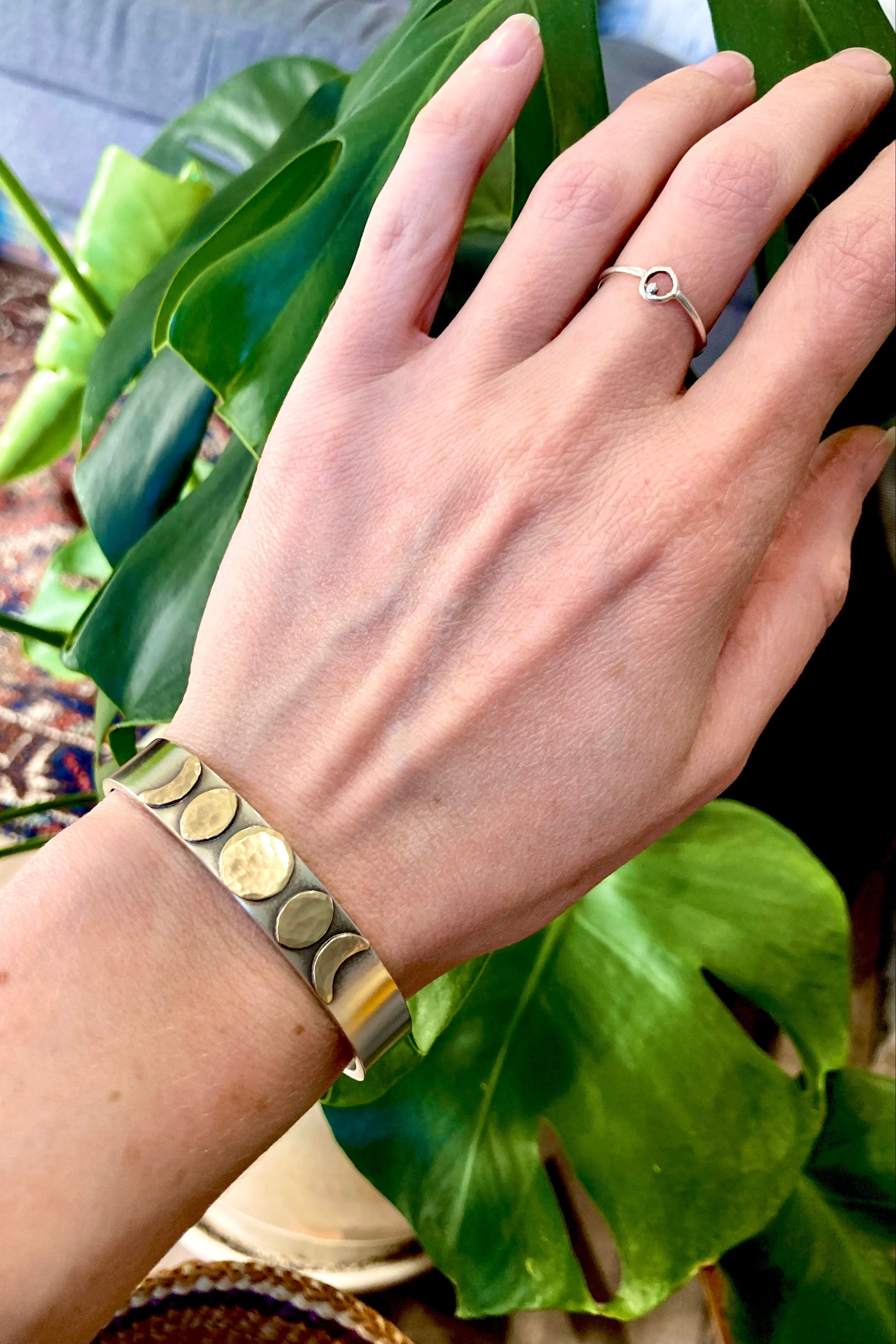 Hand wearing a gold bracelet with green leaves in the background
