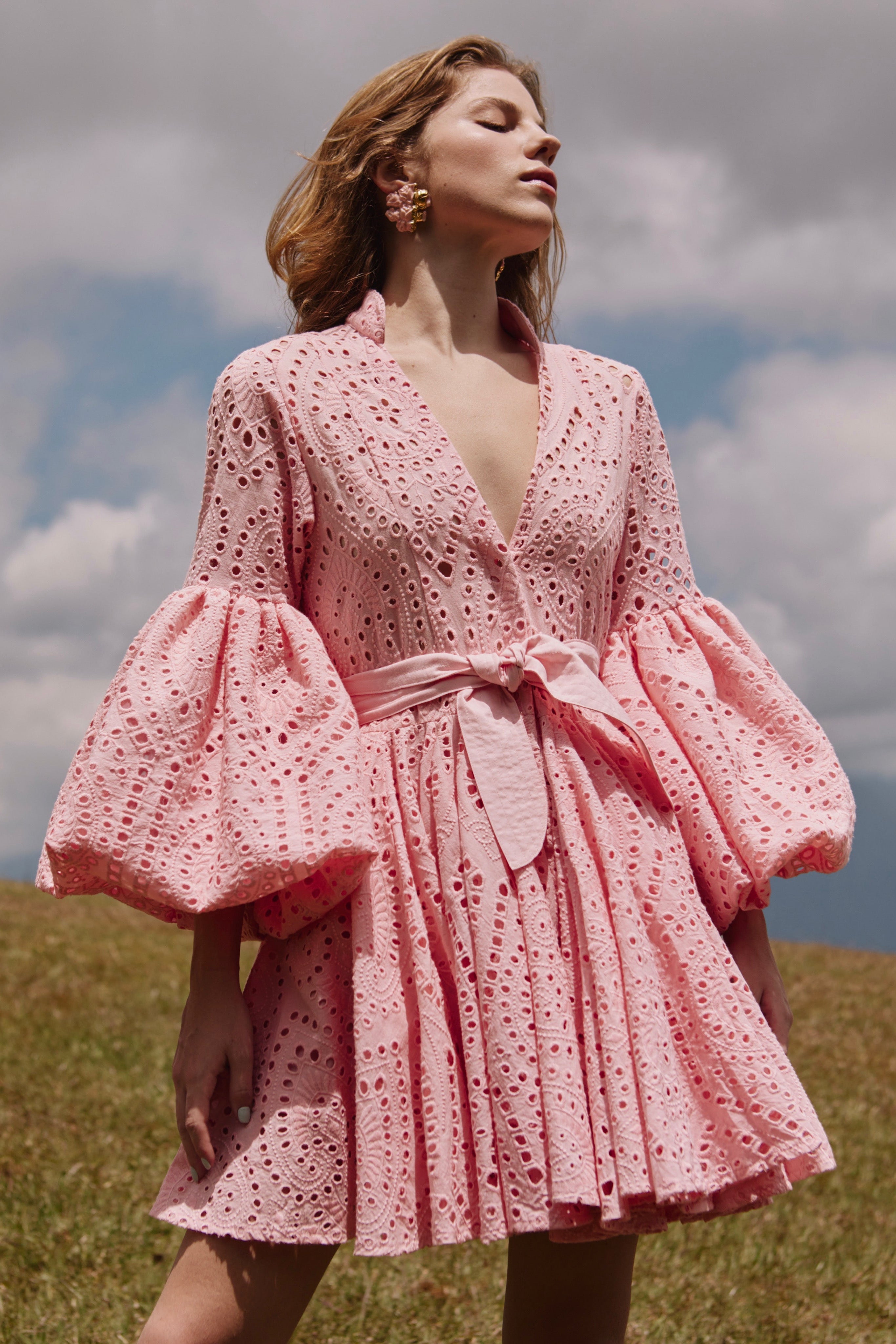 Woman wearing a pink dress with puffed sleeves against a cloudy sky.