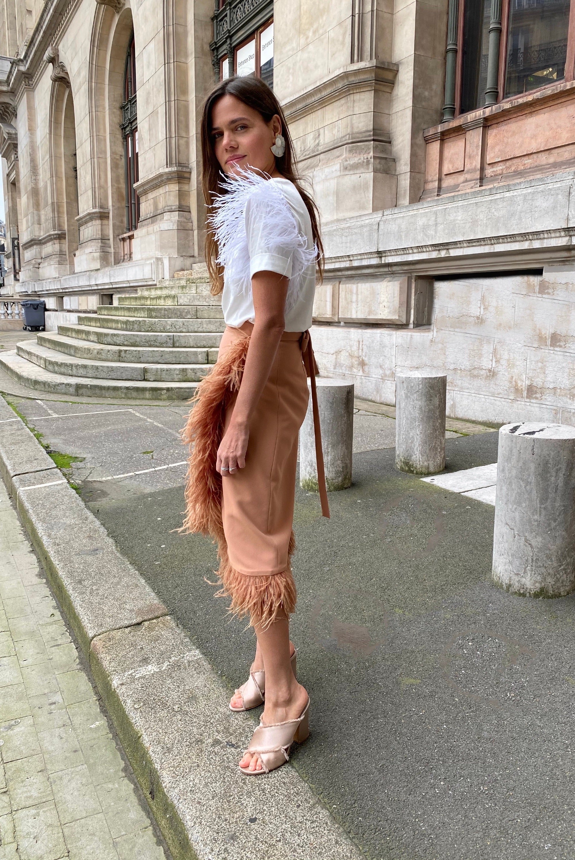 Woman in a white top and beige skirt with fringe standing on a city street.