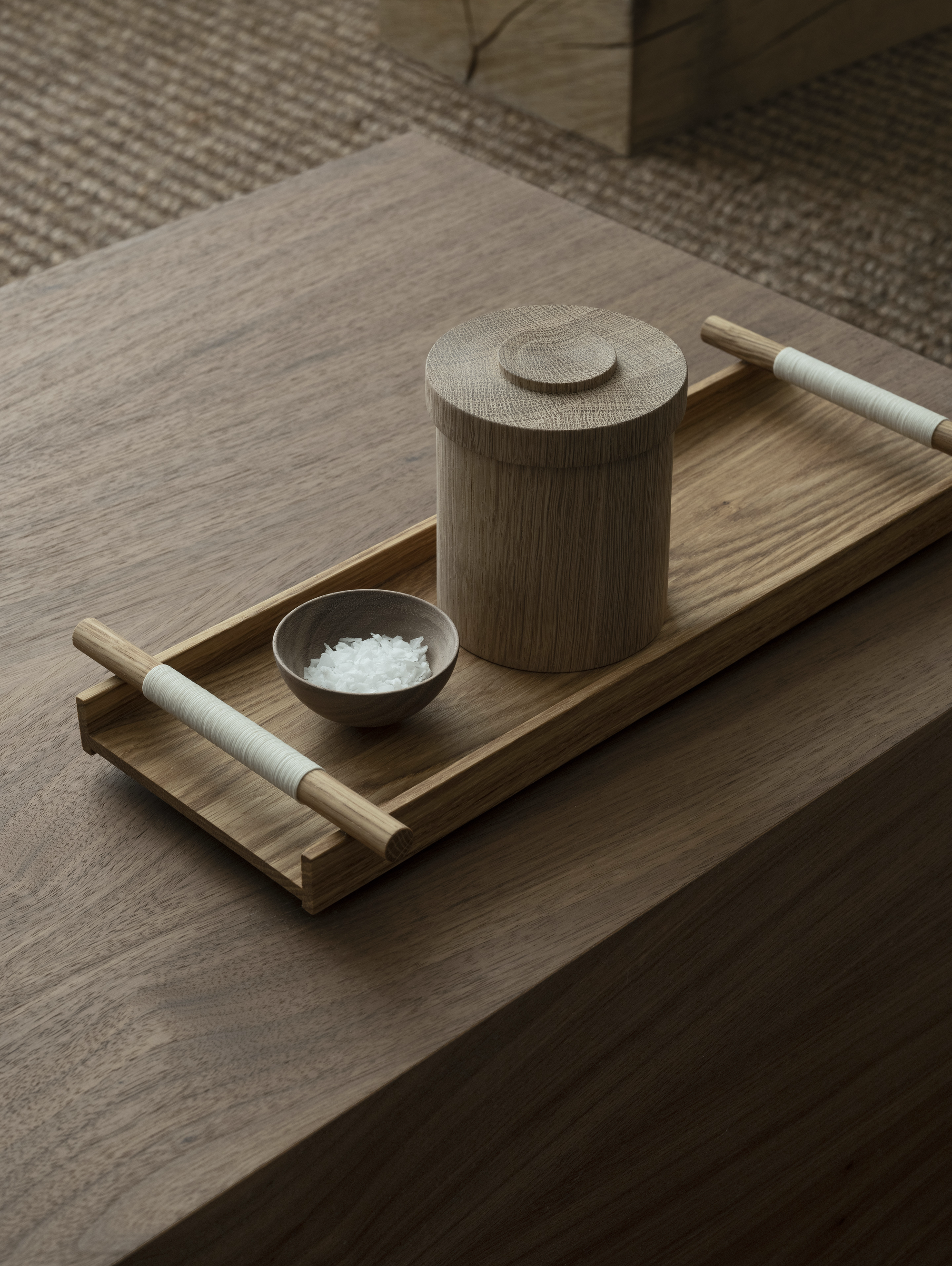 Wooden tray with a cylindrical container and small bowl on a wooden surface.