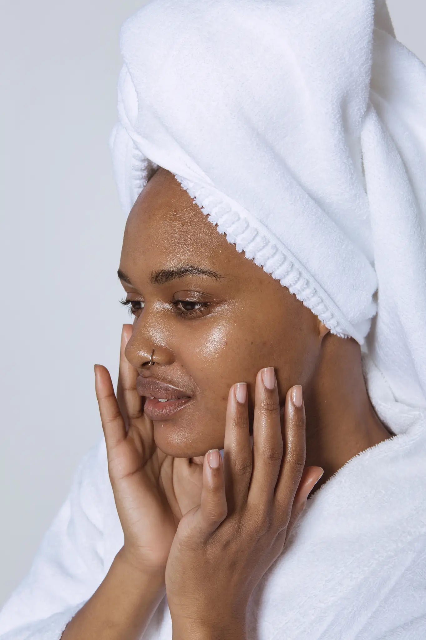Woman with a towel wrapped around her head, touching her face against a white background