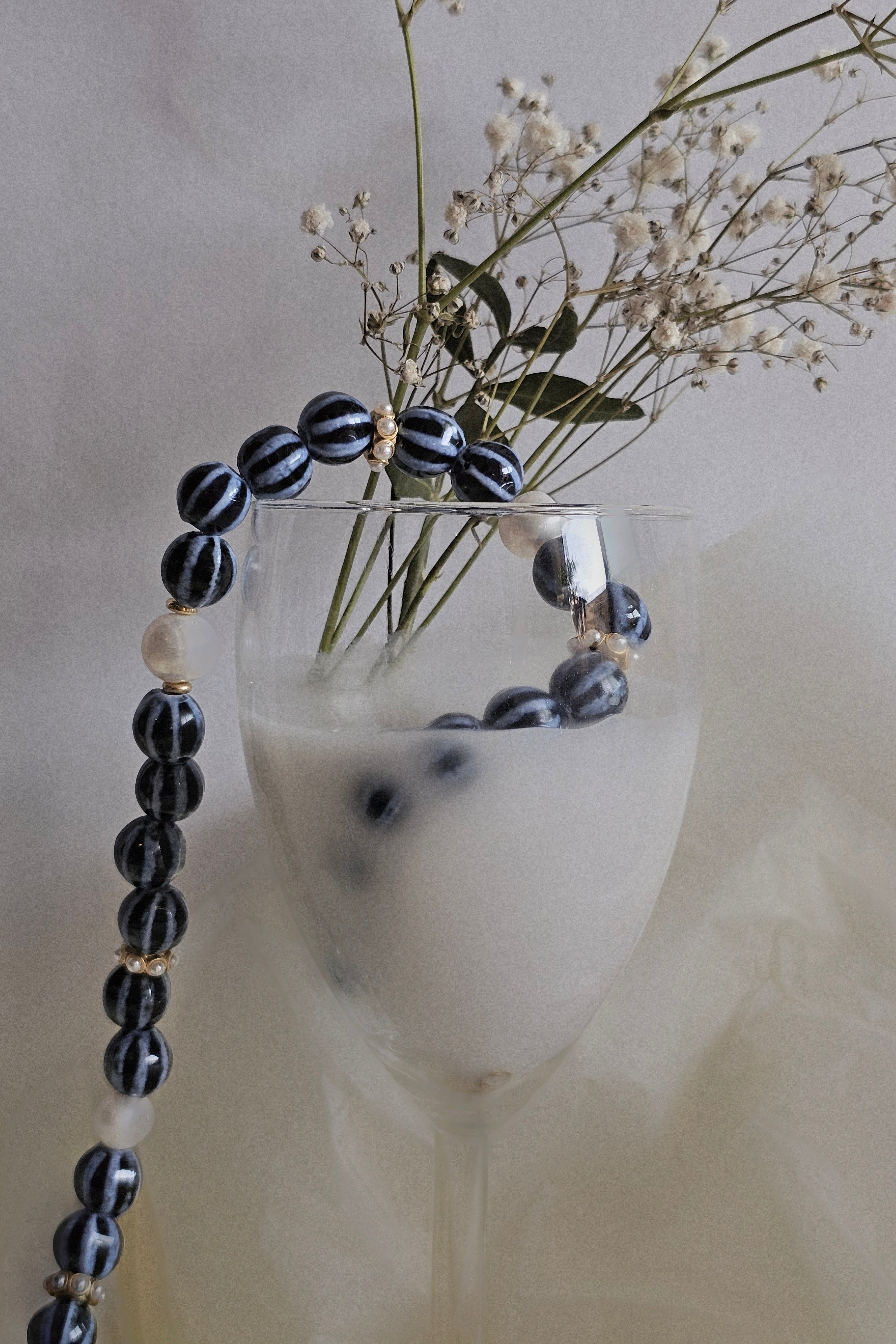 Black and white beaded necklace draped over a glass with flowers on a neutral background