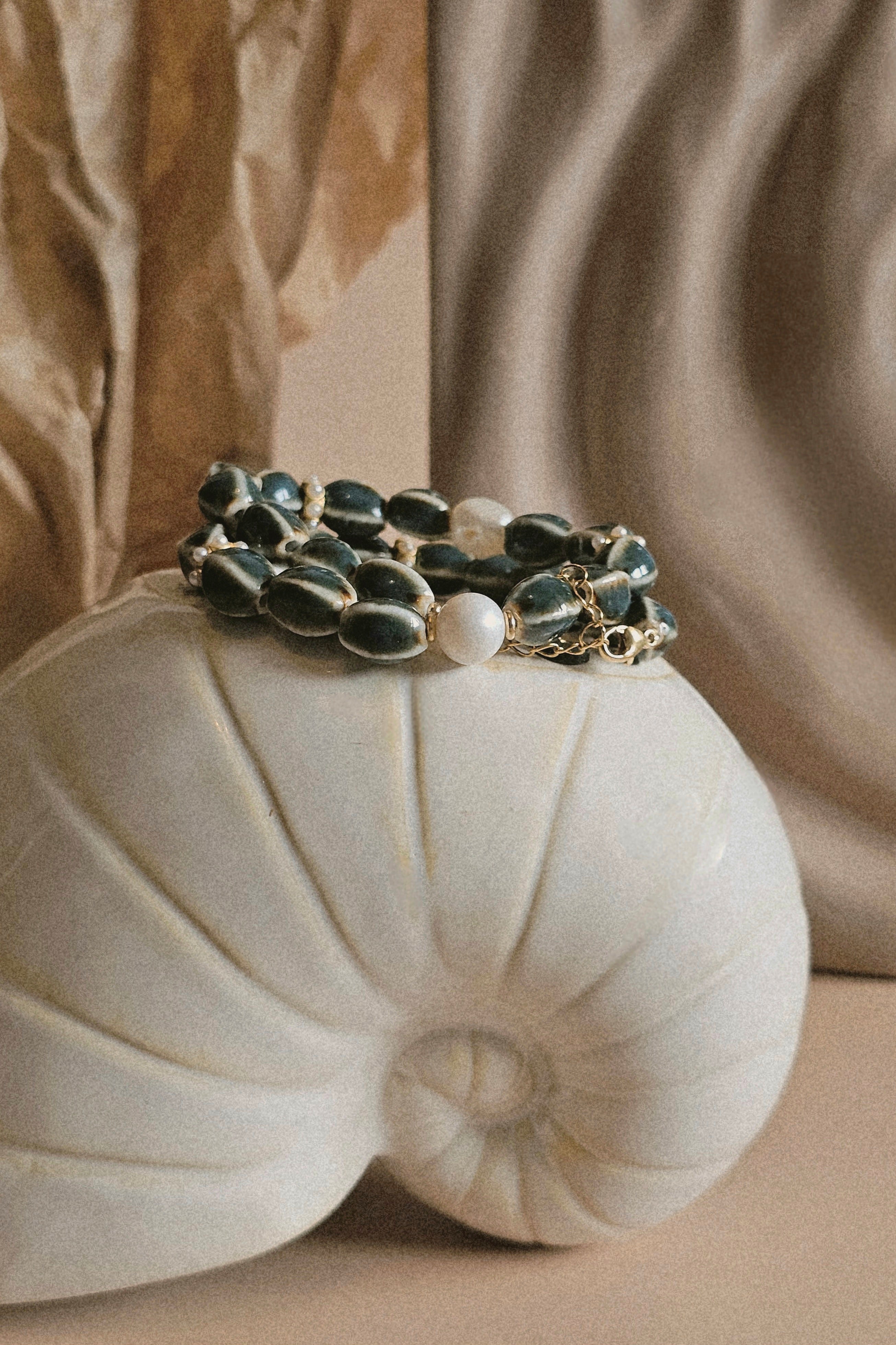 Bracelet with green stones and pearls on a shell against a beige fabric background
