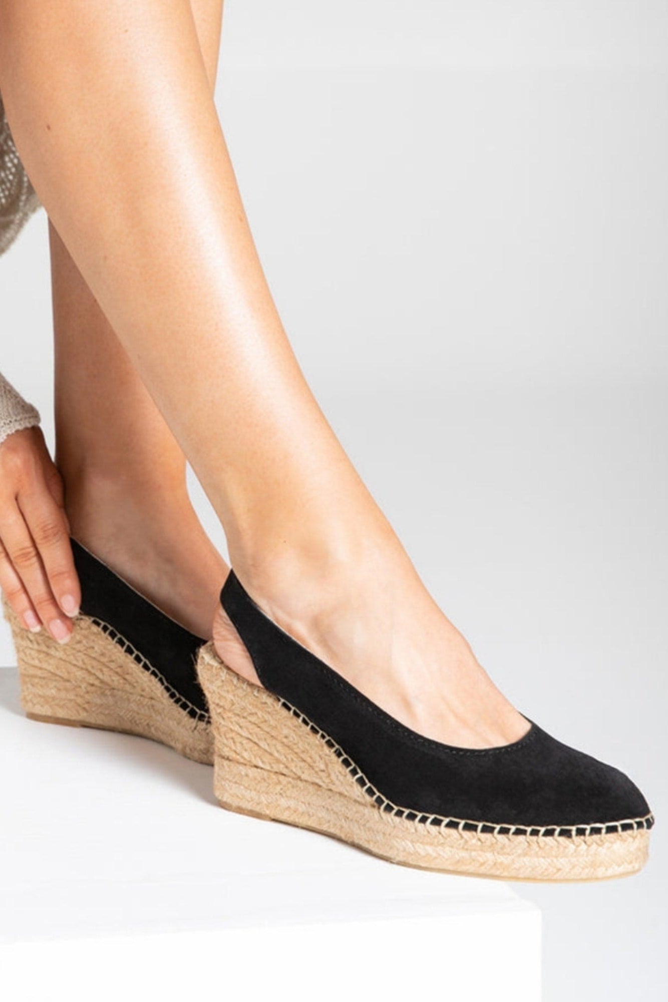 Black wedge sandals with jute sole worn by a person on a white background