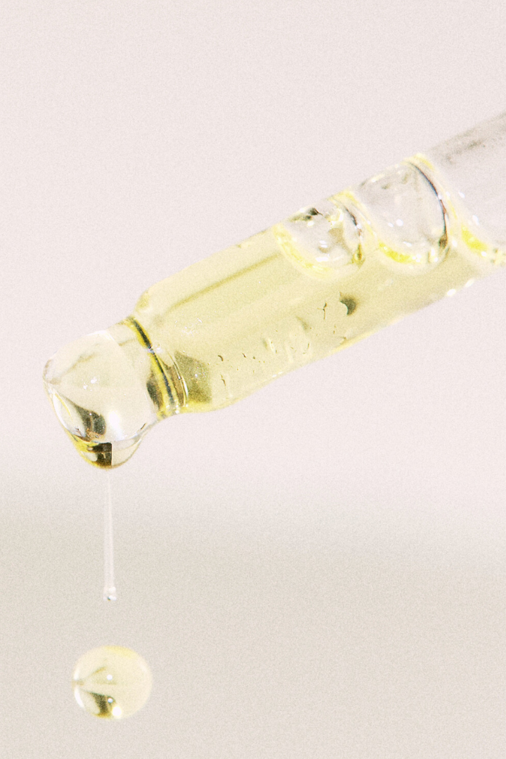 Glass dropper with yellow liquid on a light gray background