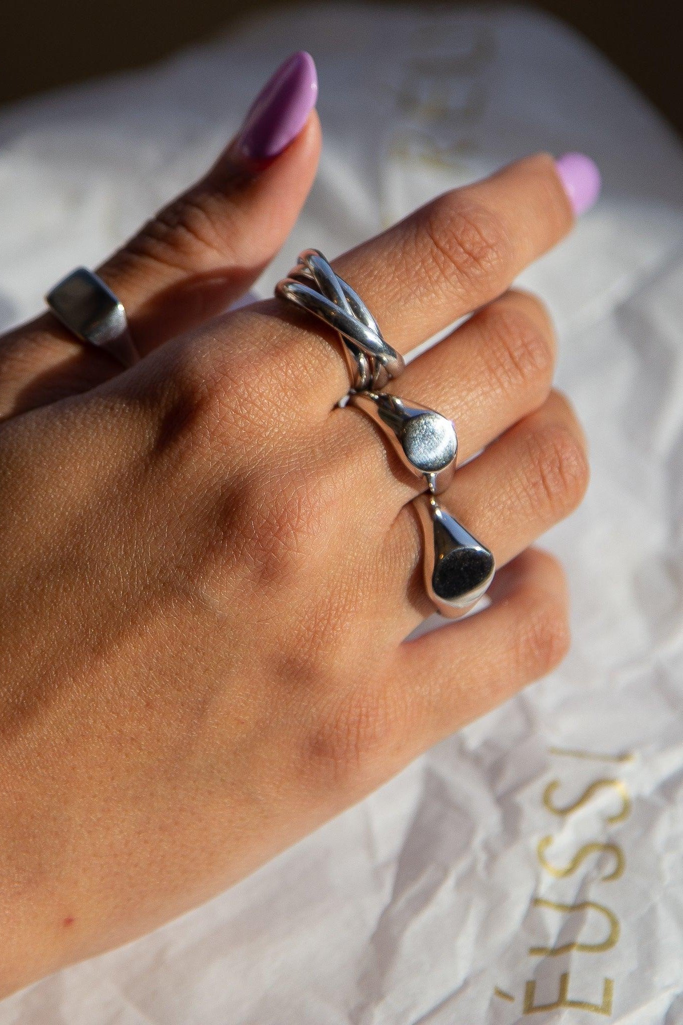 Hand wearing two silver rings on a white surface with Reussi branding.