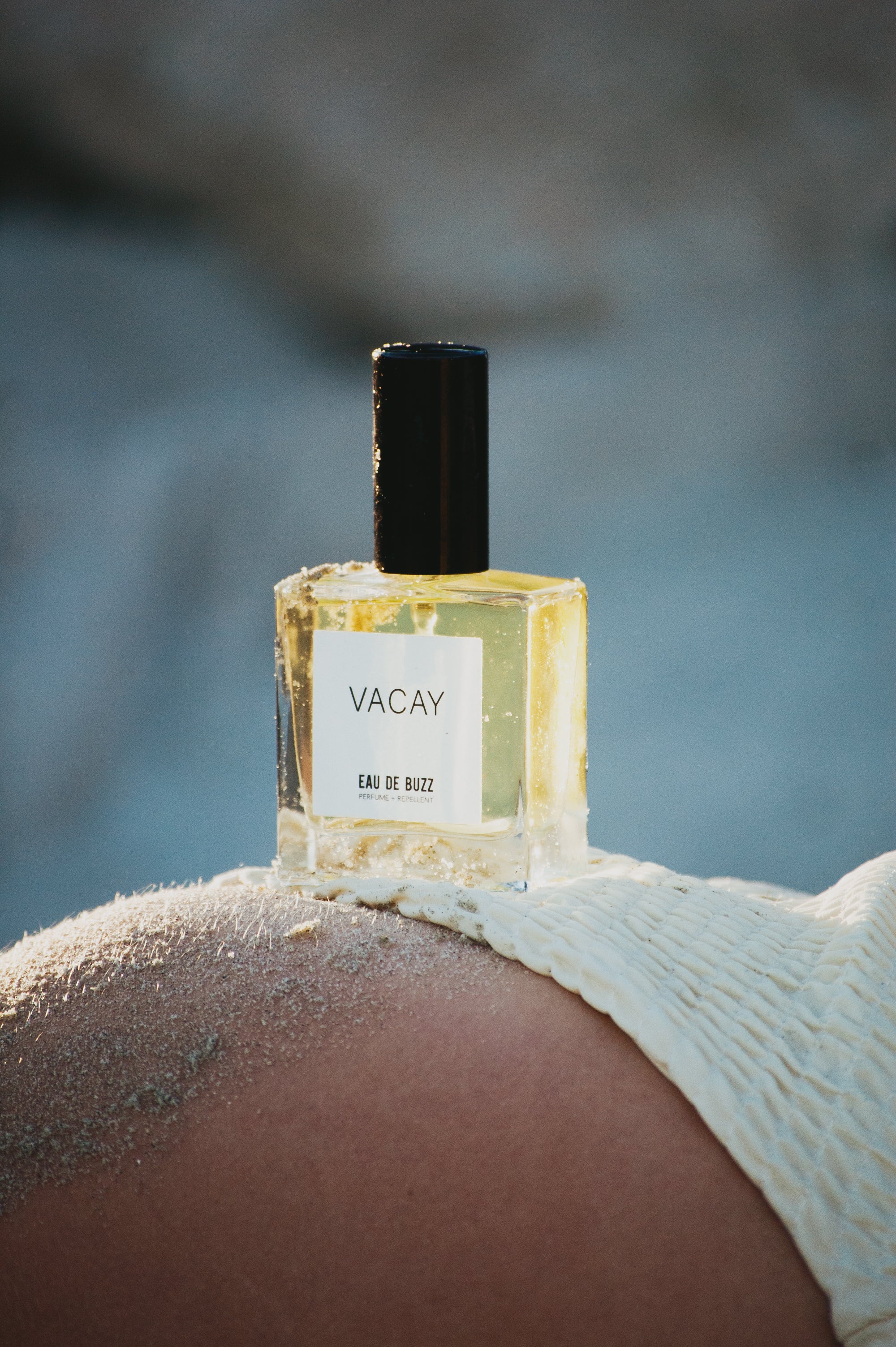 Perfume bottle labeled 'Vacay' on a beach setting