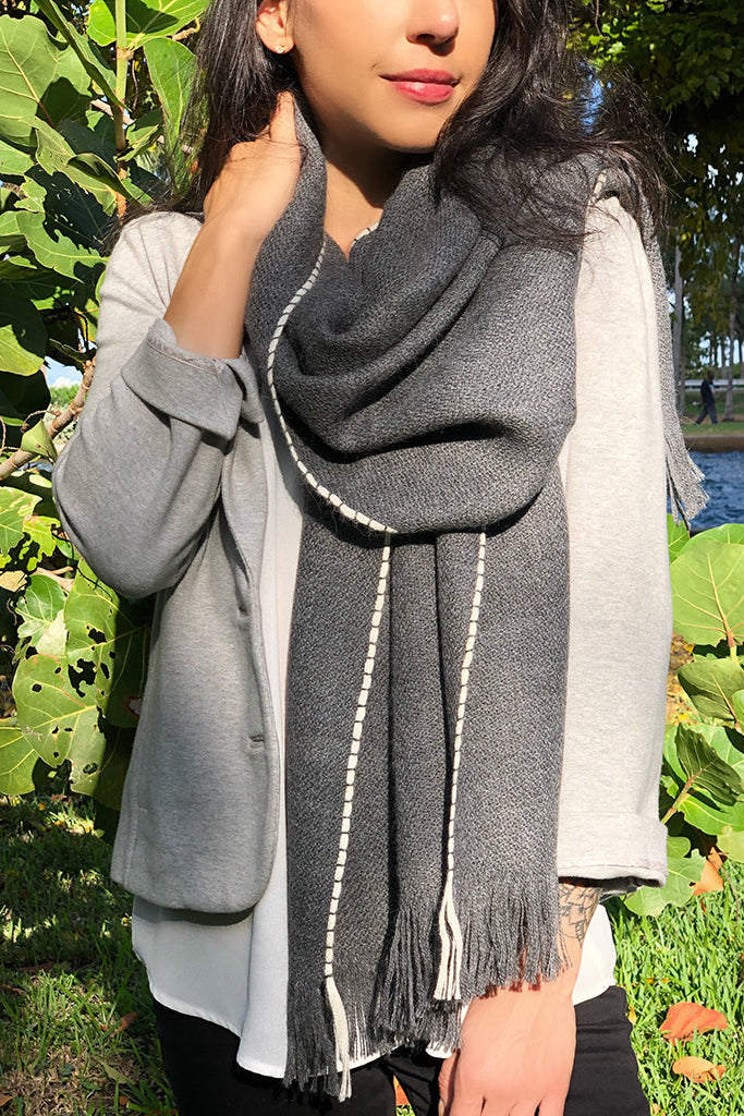 Person wearing a gray scarf outdoors with greenery in the background