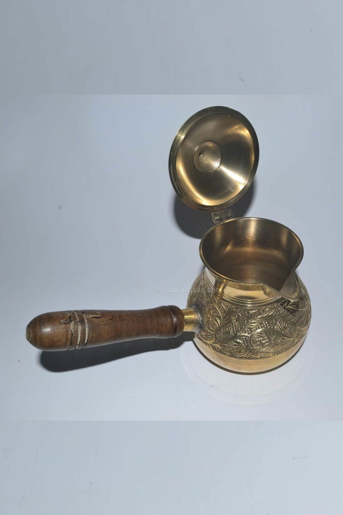 Brass turkish coffee pot with wooden handle on a light blue background.