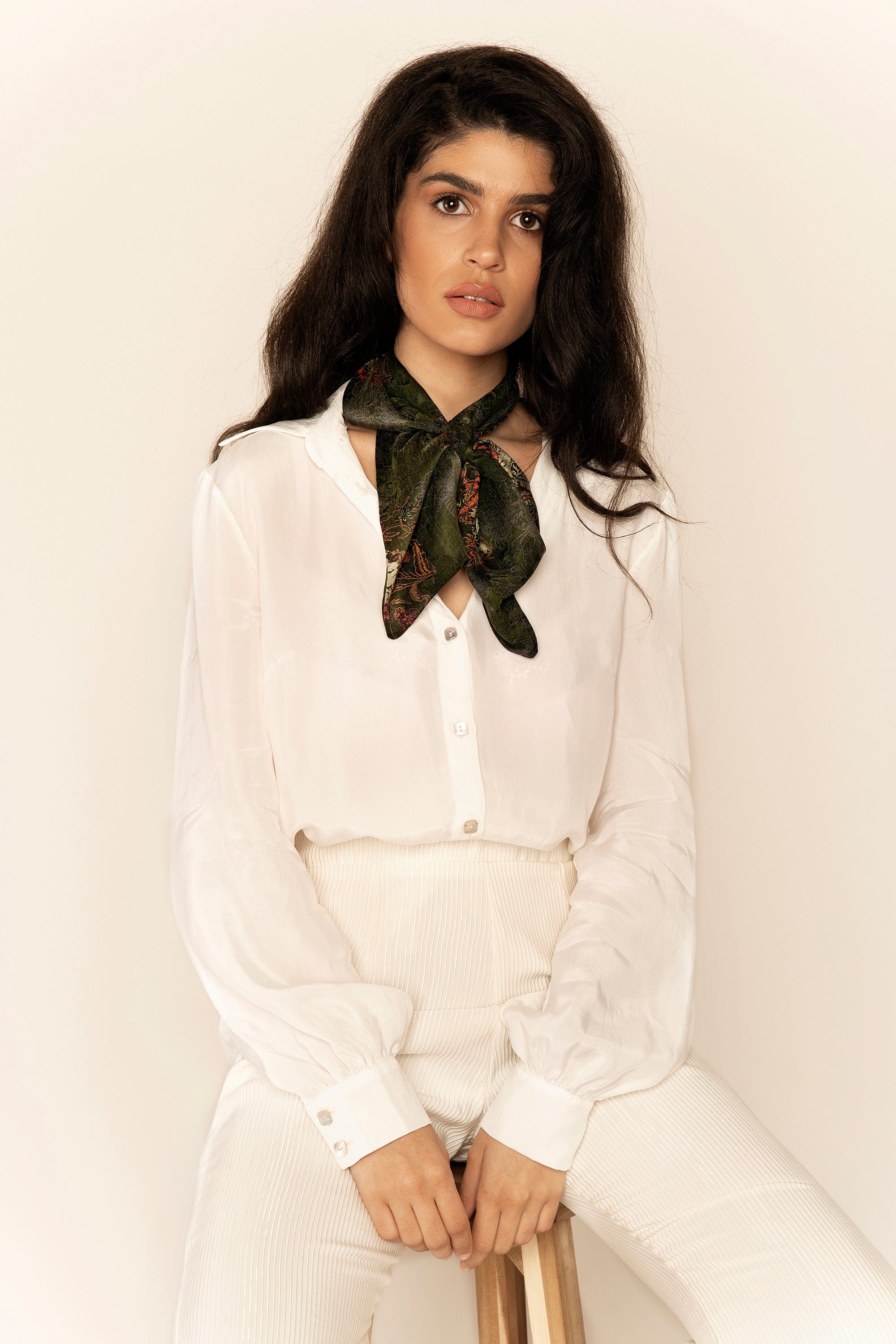 Woman wearing a white shirt and green scarf against a plain background