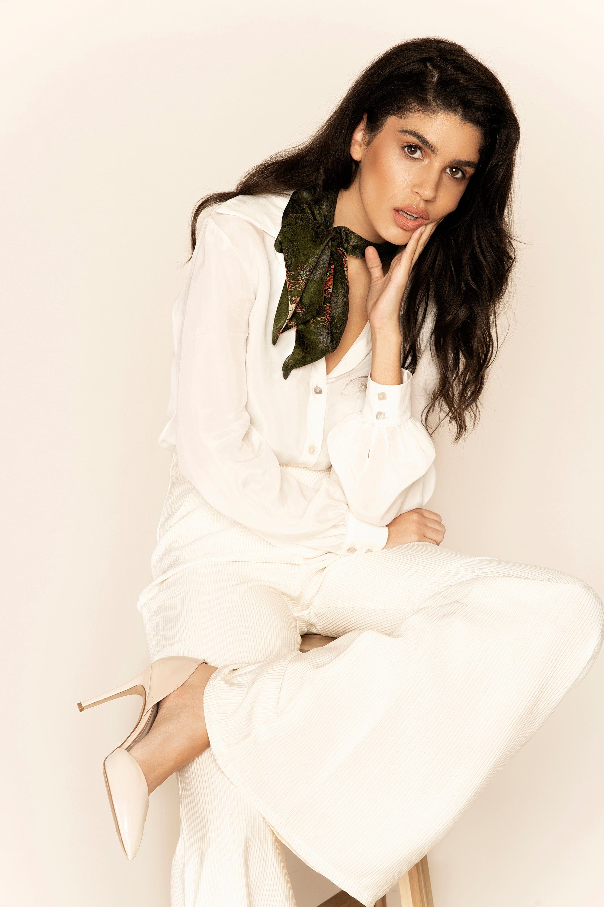 Woman in a white outfit with a black scarf against a plain background