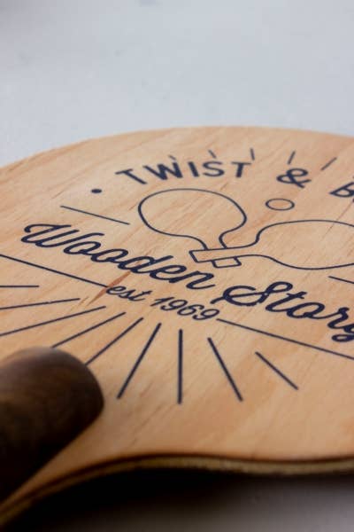 Wooden paddle with engraved text and logo on a light background